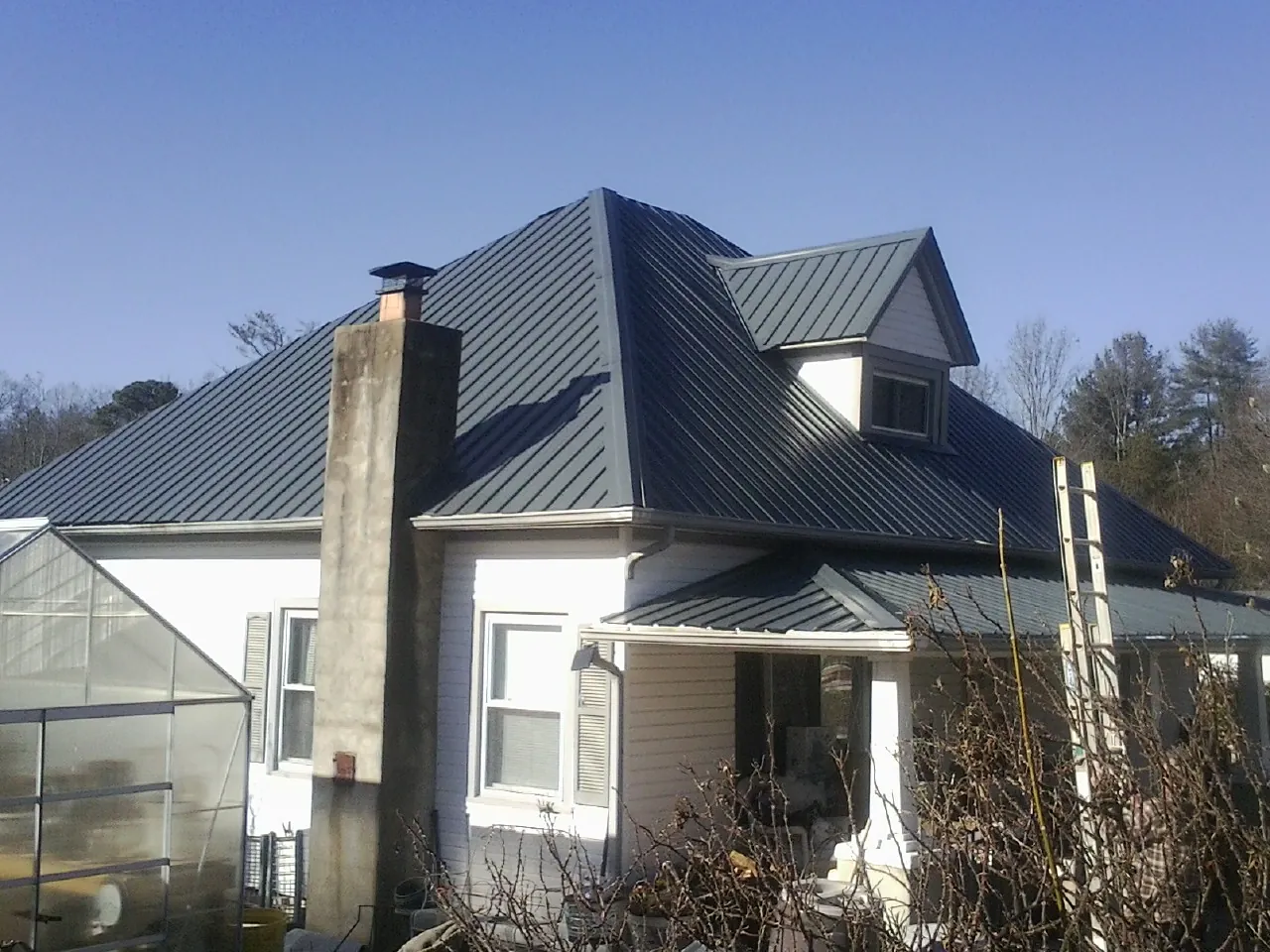 Dark blue standing seam metal roof on a white farmhouse with dormer — Slate & Tile Roof Repair by Roofing Brothers in Loves Park