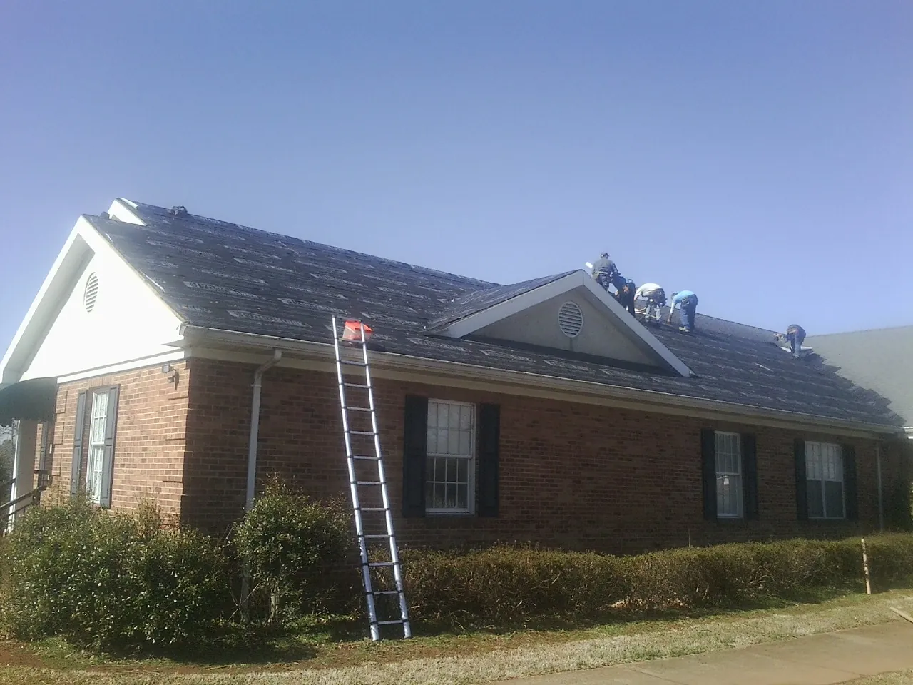 Crew tearing shingles off a brick ranch roof with a ladder set — Metal Roof Repair work by our crew in Loves Park