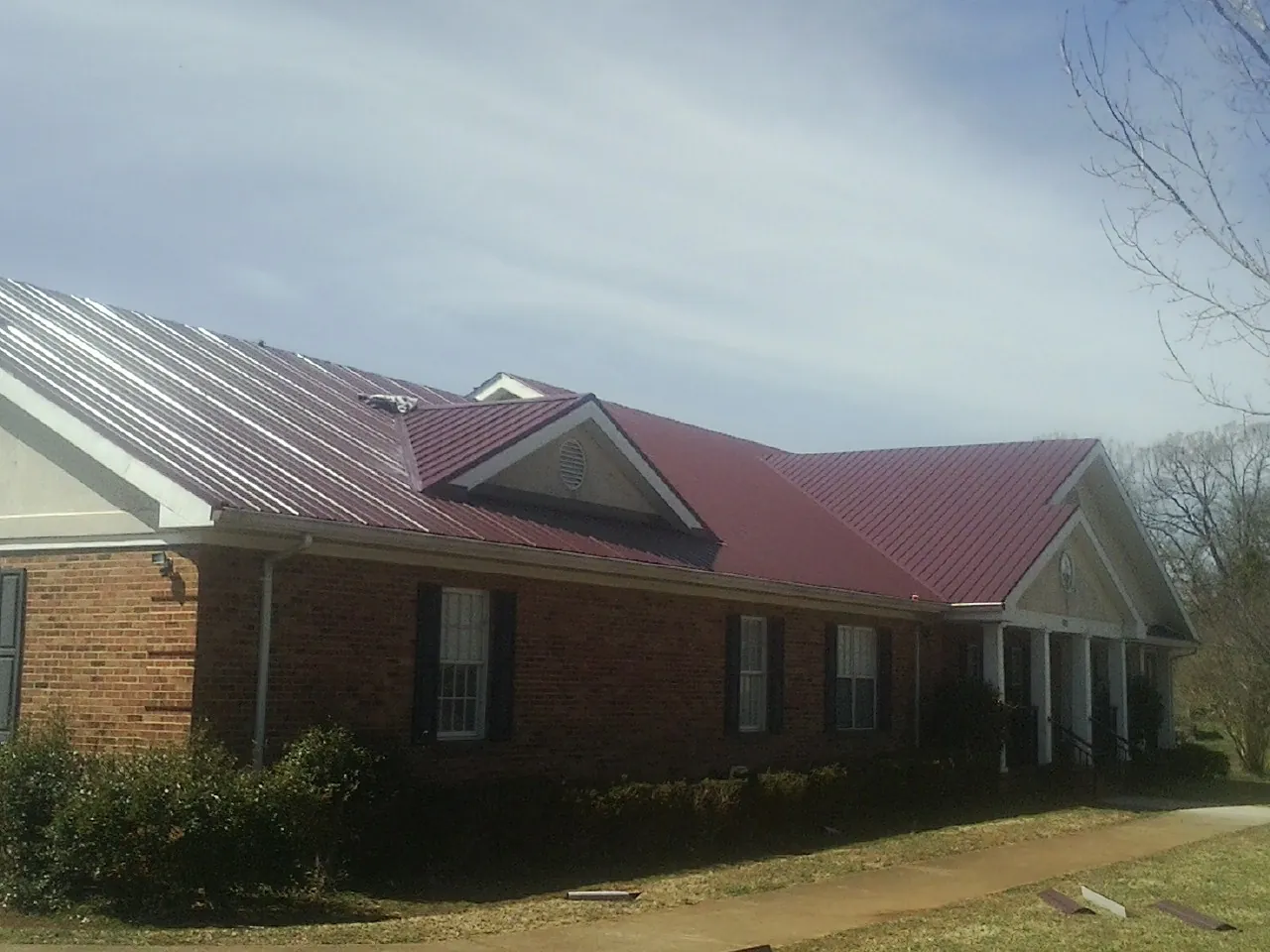 Red metal roof with gabled entries on a long brick building, from a Hail Damage Roof Repair job in Loves Park