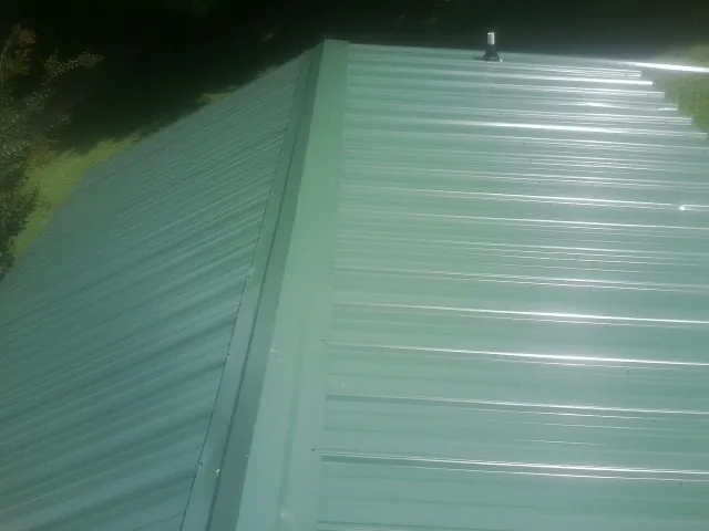 New green metal panels meeting at the ridge of a roof — Flat Roof Repair work by our crew in Loves Park
