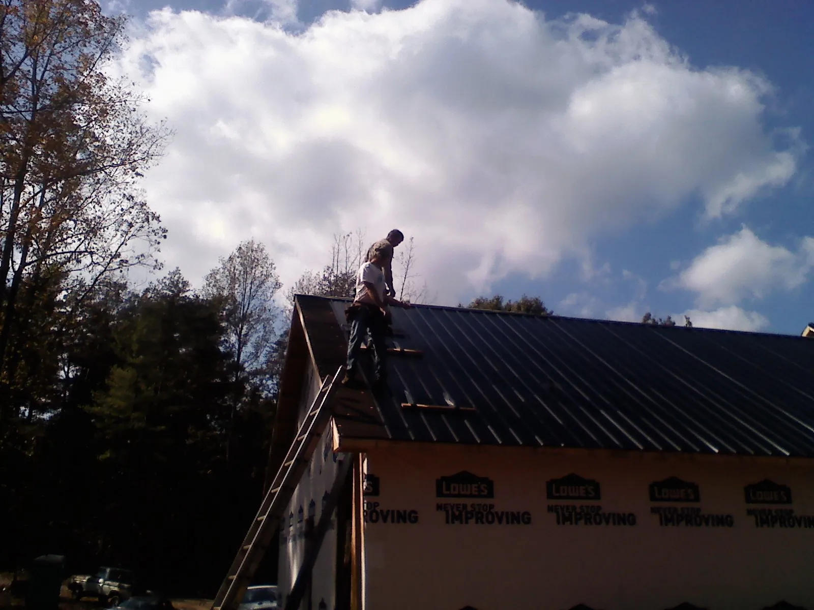 Roofer fastening dark metal panels high against a cloudy sky, from a Roof Inspection job in Loves Park