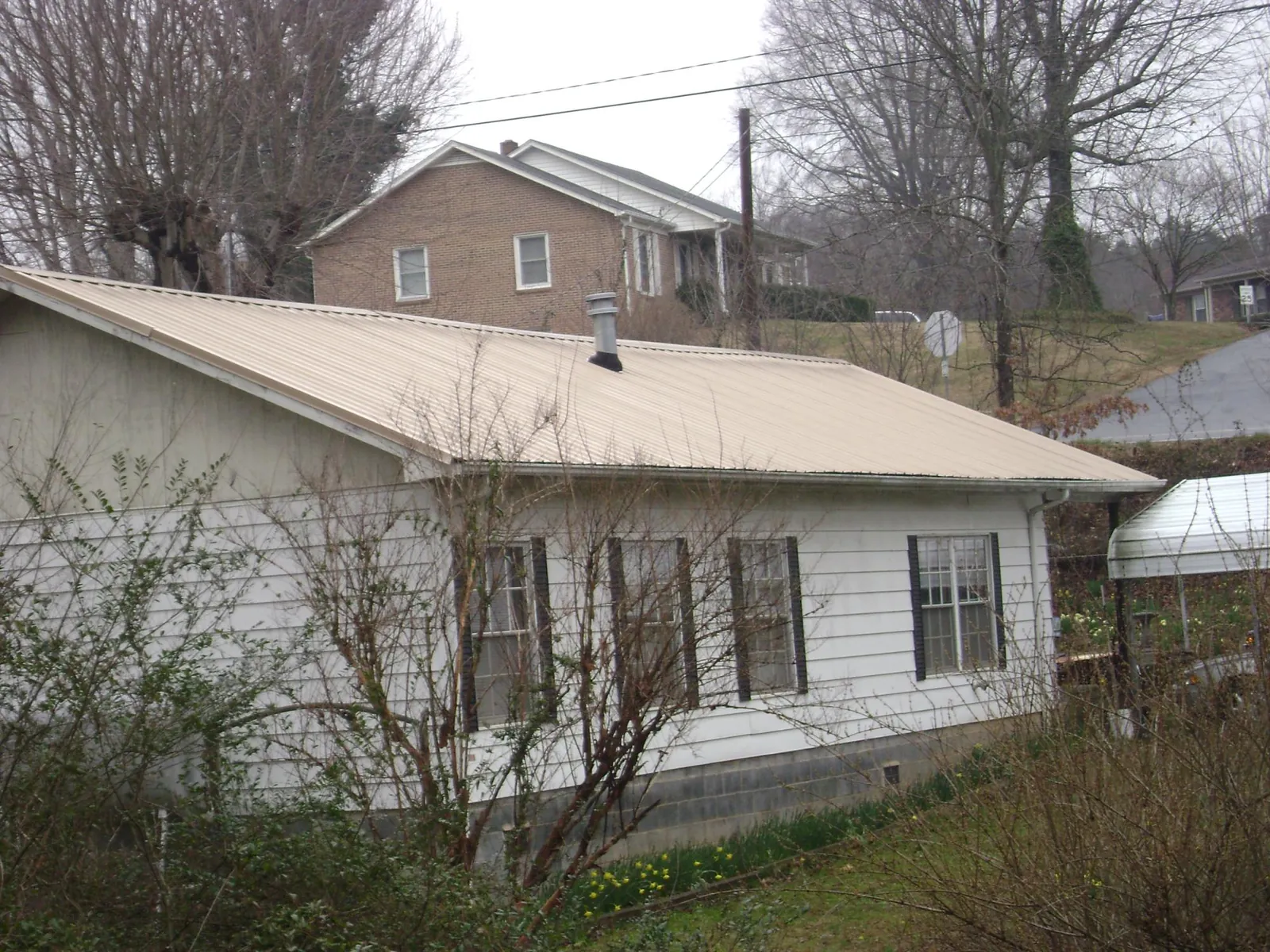 Tan metal roof on a white sided house set into a hillside — Commercial Roofing by Roofing Brothers in Loves Park