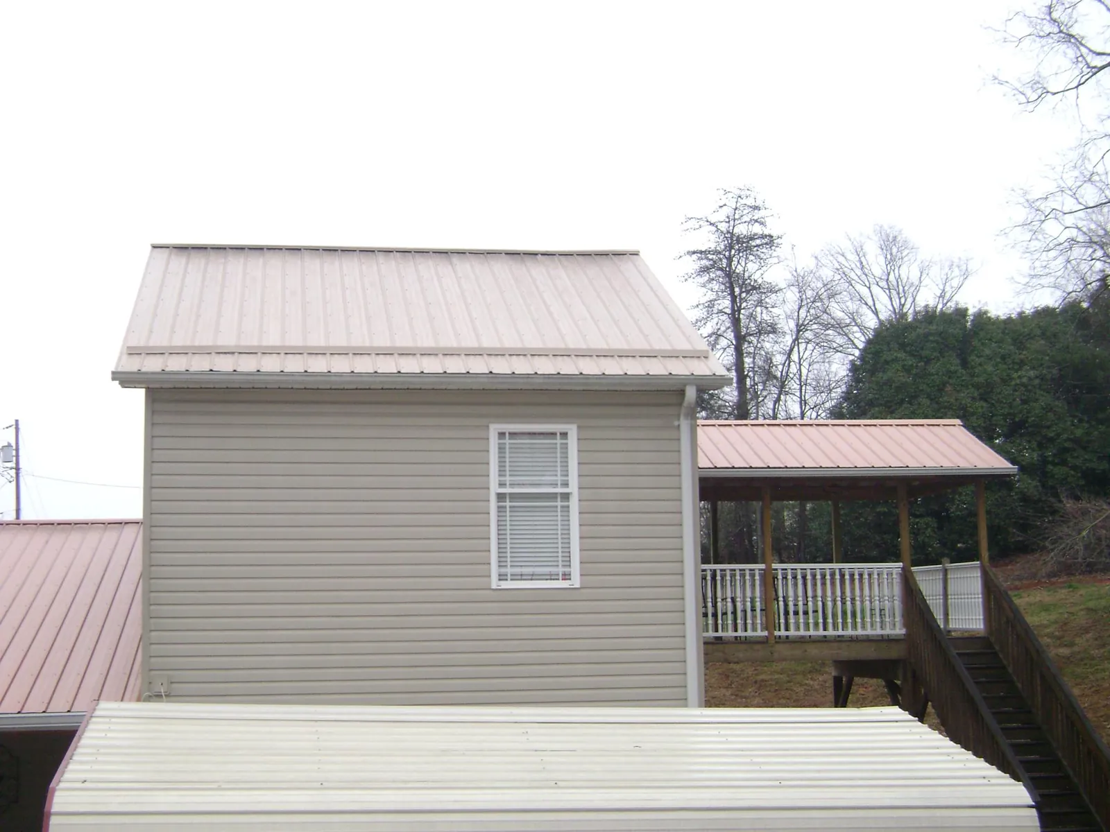 Tan metal roofs on a two story addition and attached porch, from a Roof Replacement job in Loves Park